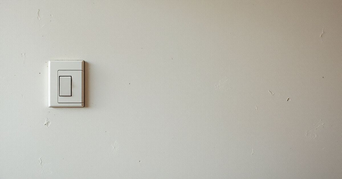 An intact apartment wall showing only faint scuffs and faded paint beside a light switch